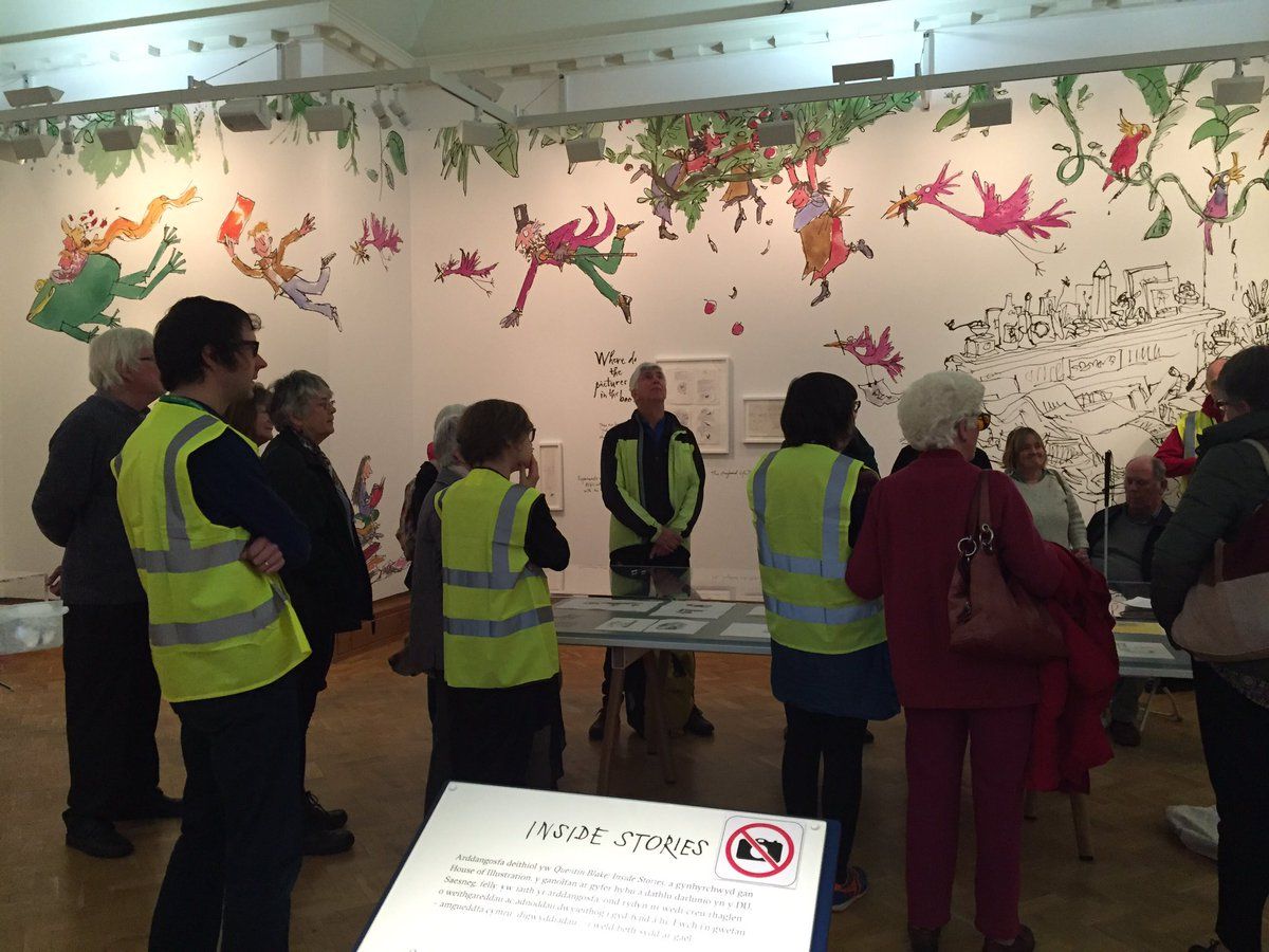 Photograph of a group of people in an art gallery listening to a guide describing an illustration