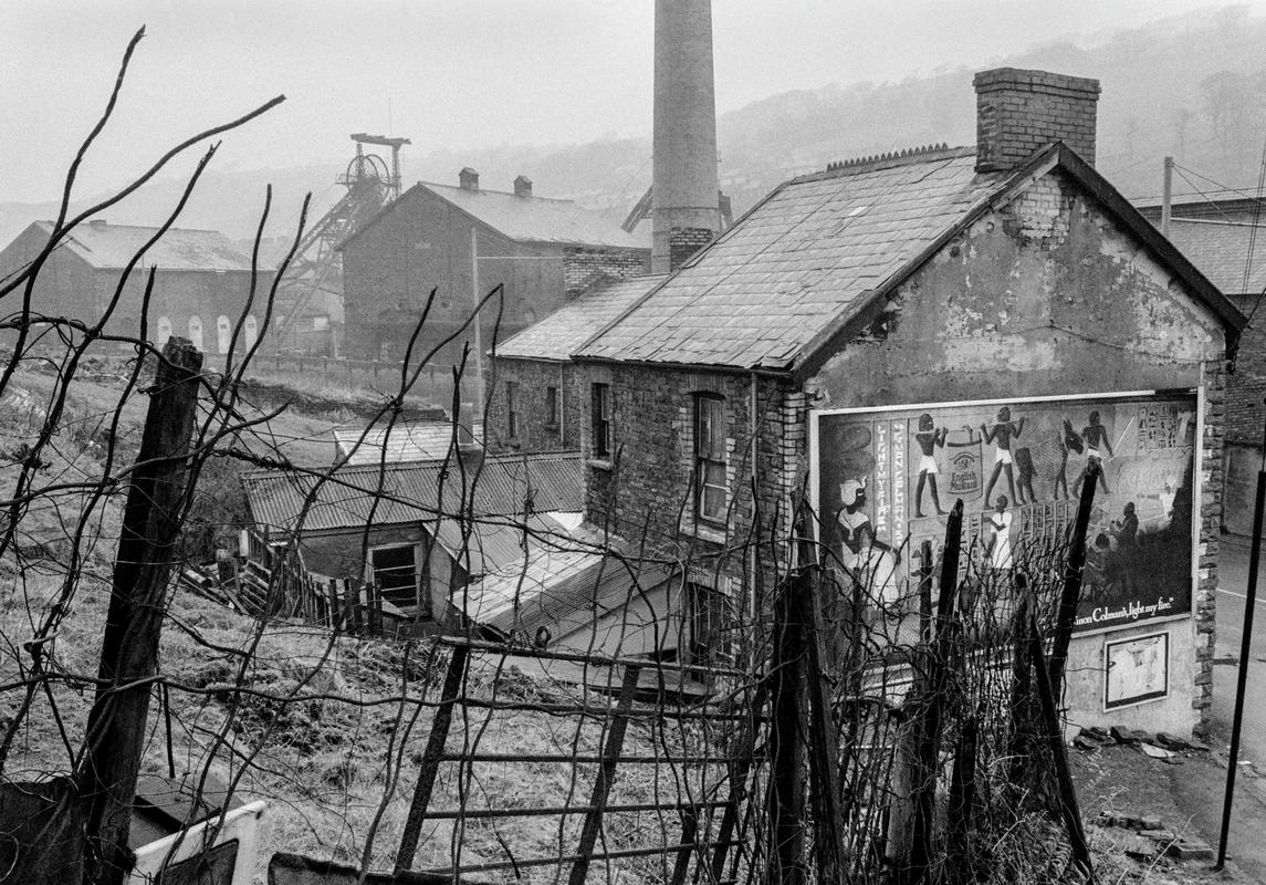 GB. WALES. Trehafod.  A poster advertisement, actually showing a period in the decline of the Egyptian Culture, symbolises the invasion of Welsh culture by the new capitalism.  The fence is made of old steel rope from the Lewis Merthr Pit seen in the background.  Trehafod, South Wales. 1979.