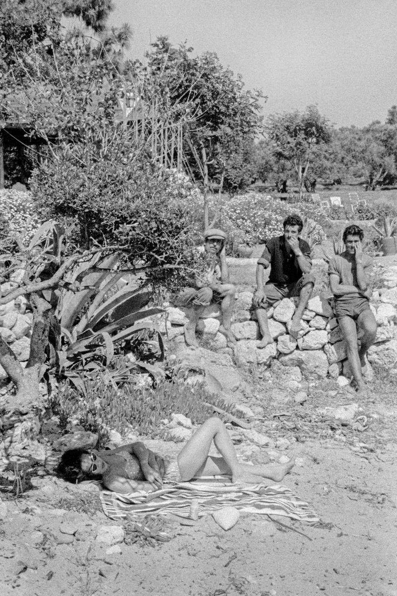 GREECE. Corfu. Paleokastritsa. Local workers admire a reader on the beach. 1964.