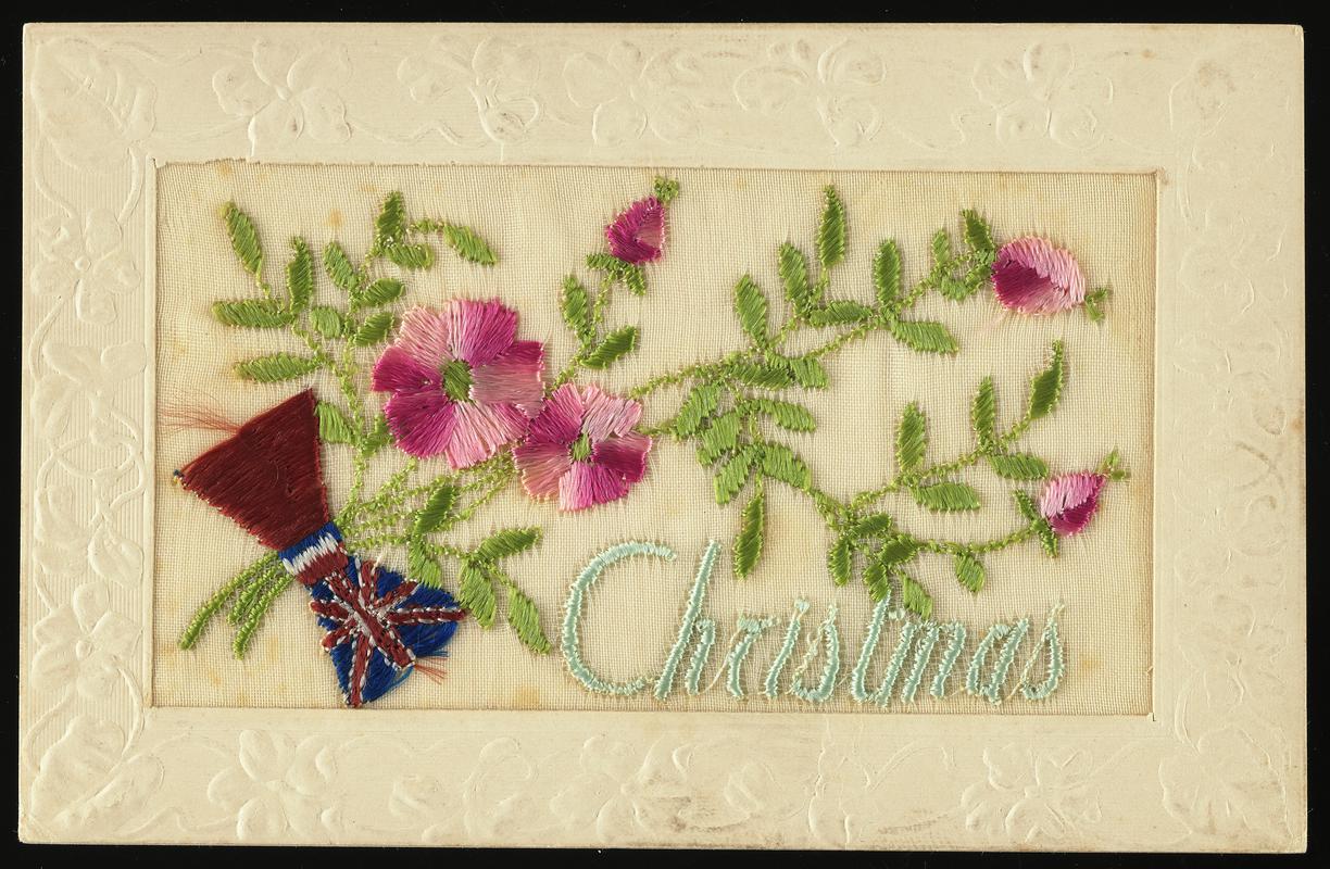 Embroidered silk postcard inscribed Christmas. Sent from France by Gordon Hobbs to his sister Hilda on 21 December 1916, during First World War. Embroidered  with pink floral motifs with a Union Jack bow. Message on back.