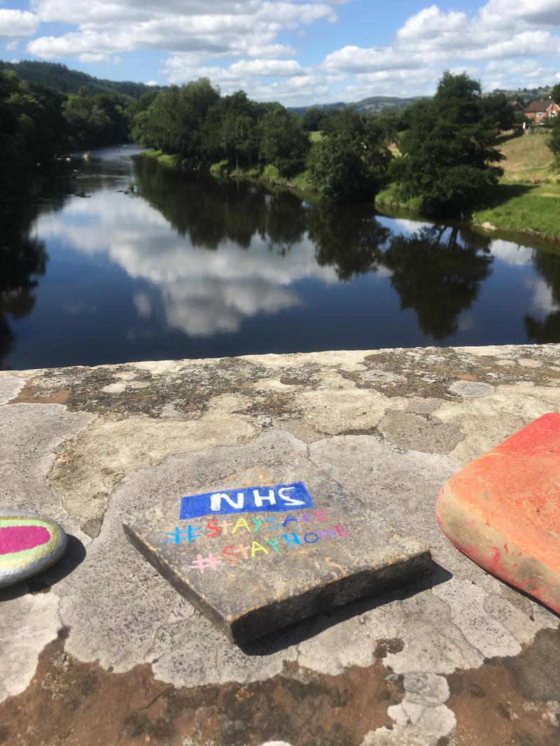 A pebble painted with the NHS logo and #Staysafe #Stayhome. On Boughrood Bridge, over the River Wye, Boughrood, Powys.