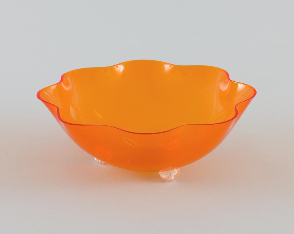 Orange plastic fluted edge fruit bowl with three clear plastic semicircle &#039;legs&#039;.