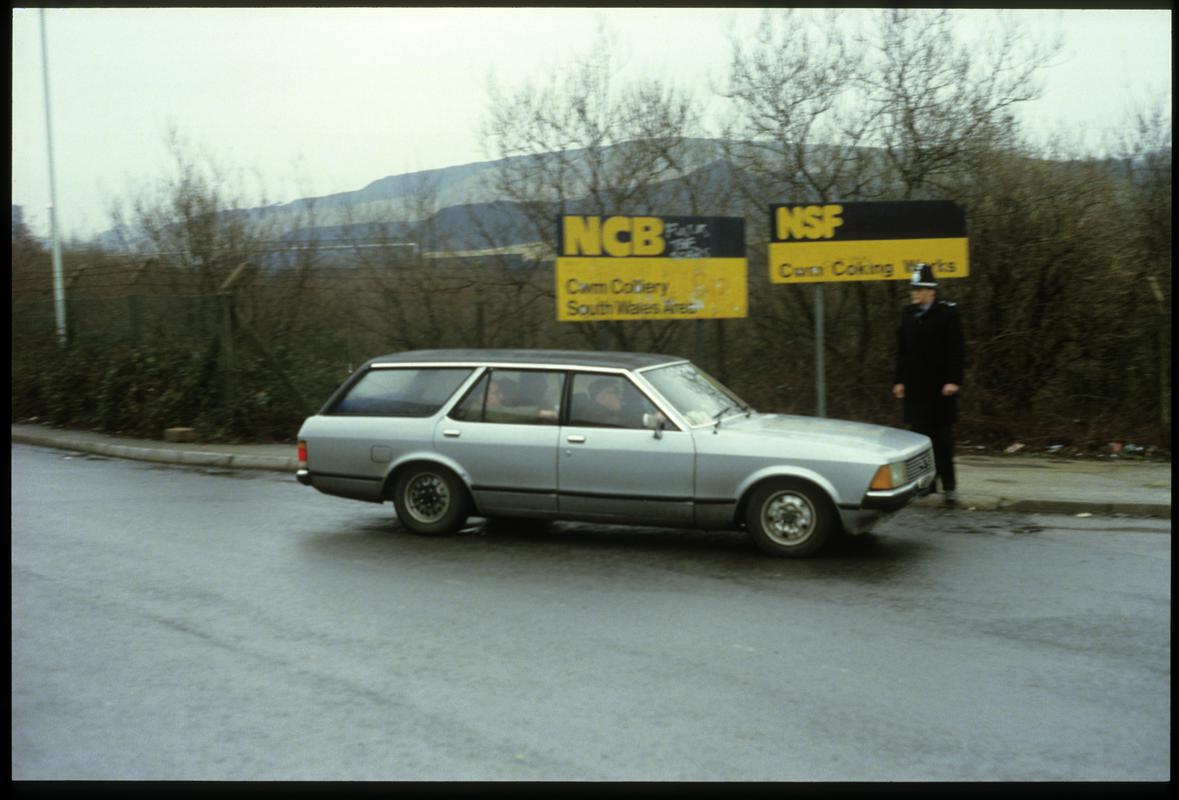 Three &#039;blackleg&#039; miners being driven home past police guard at Cwm Colliery entrance.