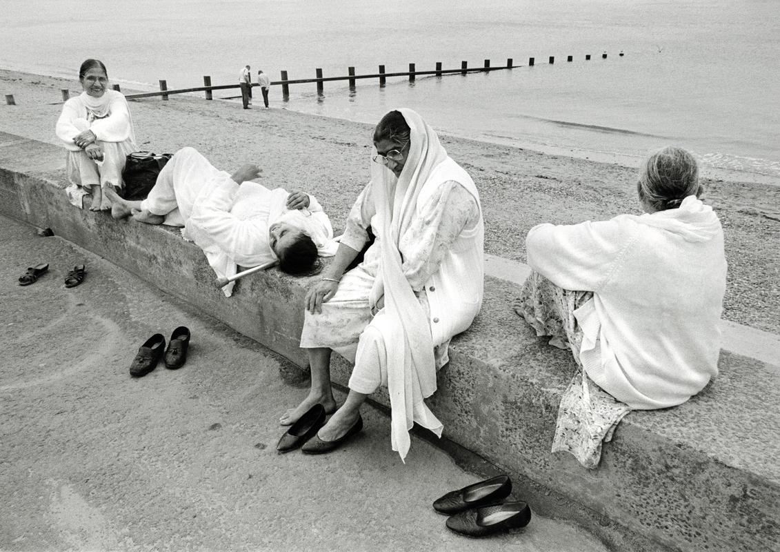 GB. WALES. Rhyl. Asian tourists from Liverpool on a day trip, sit on the wall of the sea front. 1997.