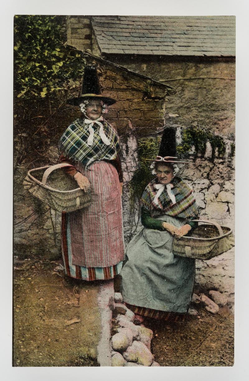 2 women in Welsh costume, each carrying a large empty basket.