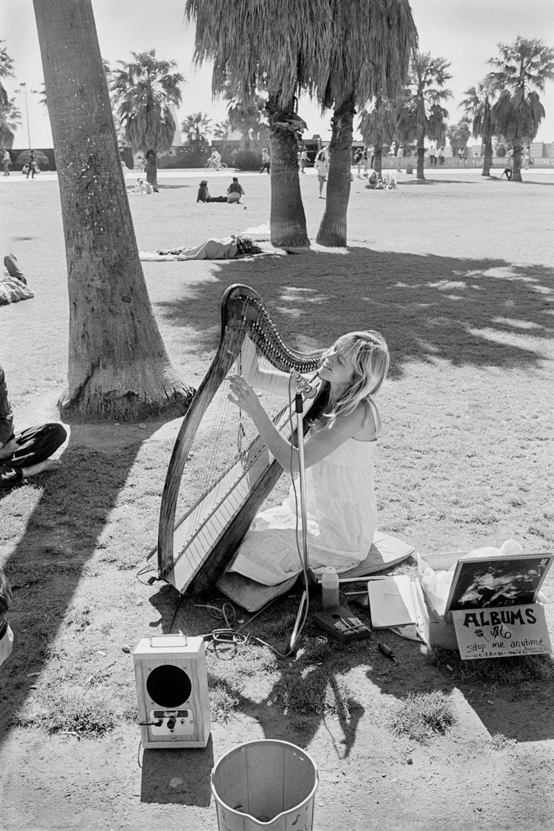 USA. CALIFORNIA. Santa Monica, Venice Beach. Girl playing the harp on promenade. 1980.