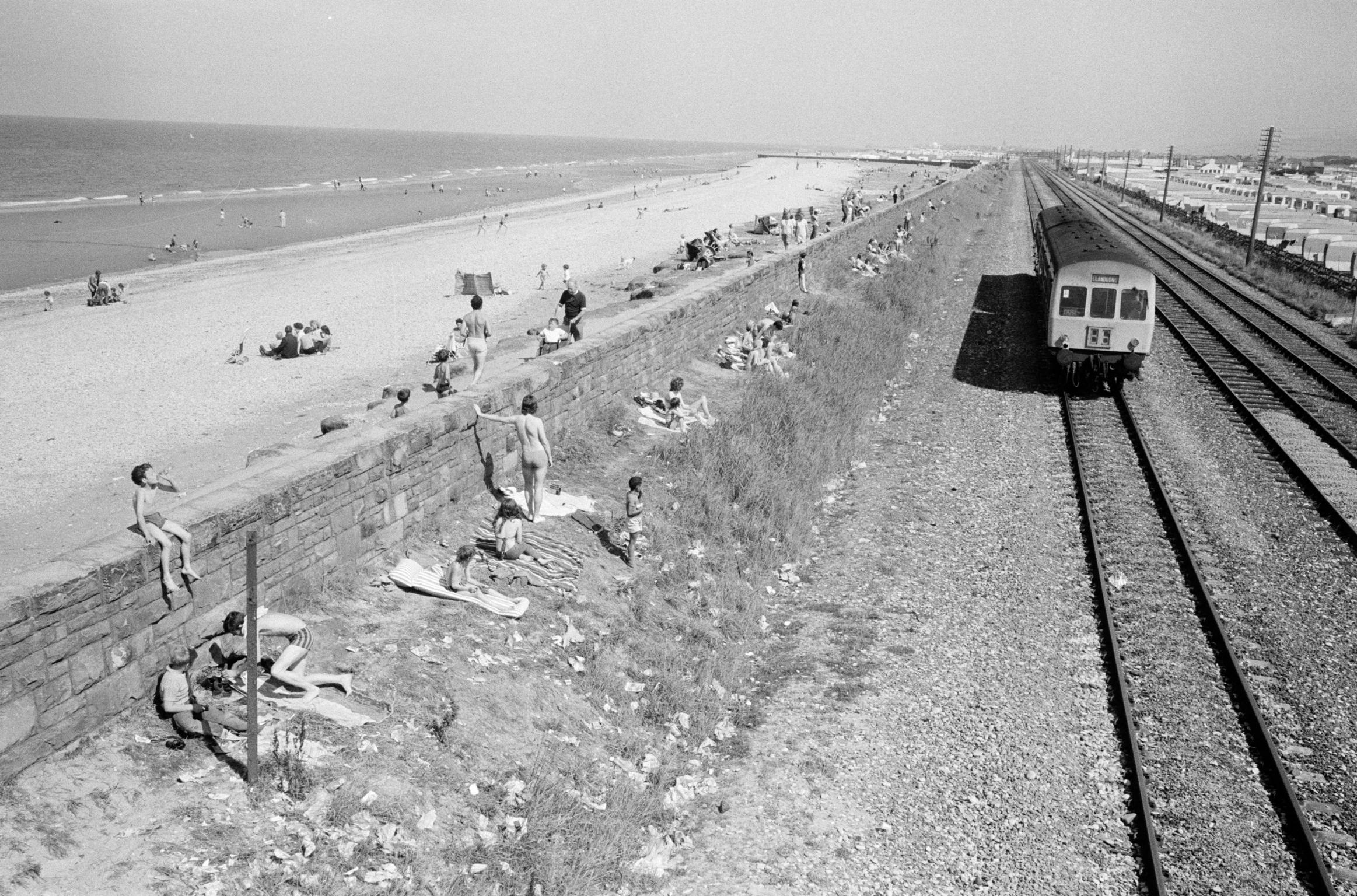 Tourists from the local caravan site shelter from the sea breezes by sun bathing on the railway bankside. Abergele, Wales