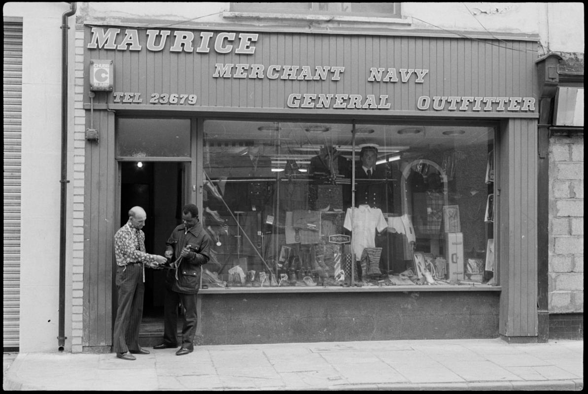 Exterior view of &#039;Maurice Merchant Navy General Outfitter&#039;, 5 James Street, Butetown, showing the proprietor Mr M. Colpstein assisting a customer.