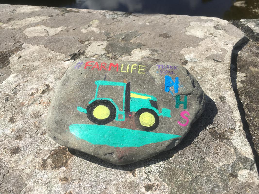 A pebble depicting a painting of a tractor and the words reading &#039;#Farmlife Thank you NHS&#039; on Boughrood Bridge, over the River Wye, Boughrood, Powys.