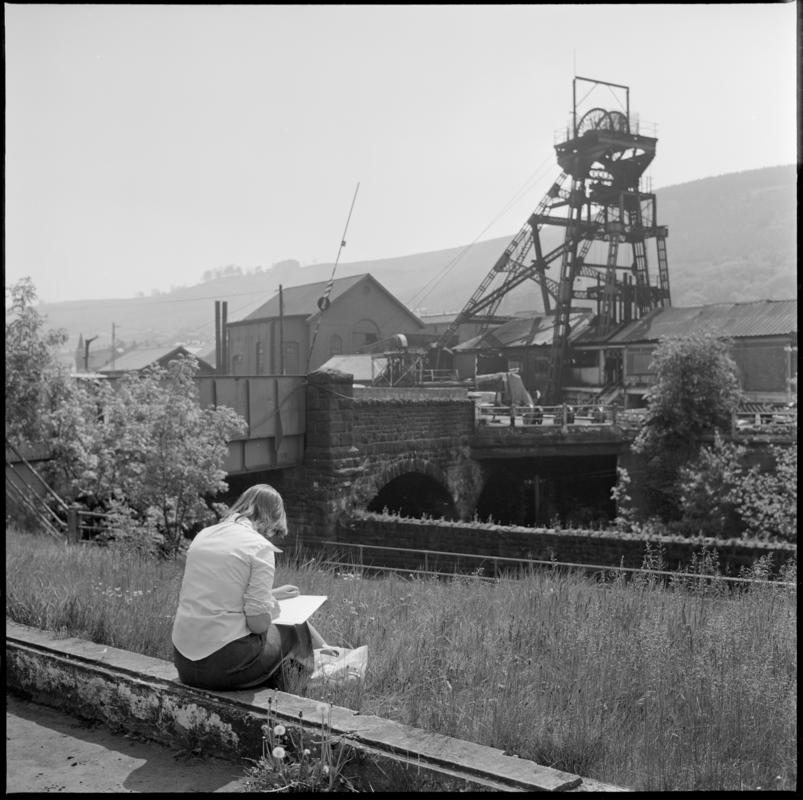 Black and white film negative showing a woman sketching a surface view of Deep Duffryn Colliery 1977.  &#039;Deep Duffryn 1977&#039; is transcribed from original negative bag.