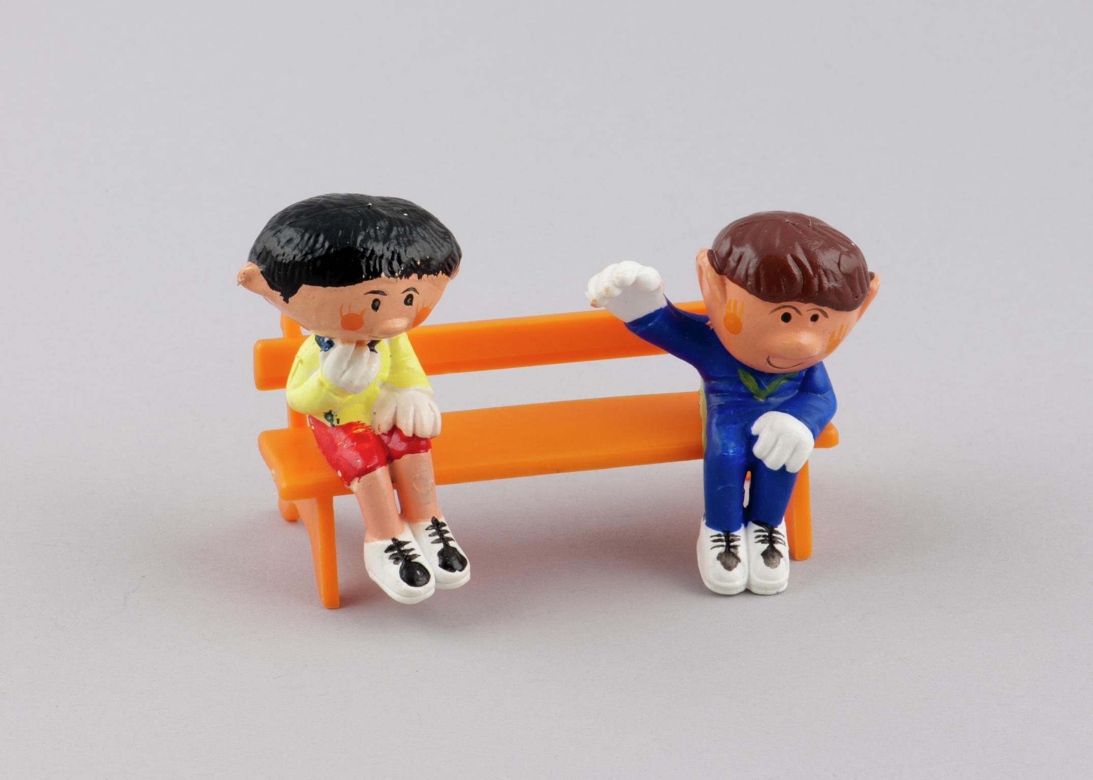 Sitting model of character Basil (2000.179/4) from the Magic Roundabout &amp; Sitting model of character Paul (2000.179.5) from the Magic Roundabout. Model of orange plastic bench (2000.179/14) with two holes on seat for figures from the Magic Roundabout to be inserted.