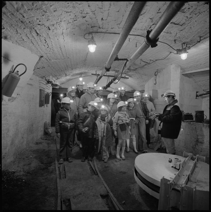 Black and white film negative showing visitors to Big Pit Mining Museum with guide near pit bottom, 1983.  &#039;Big Pit&#039; is transcribed from original negative bag.