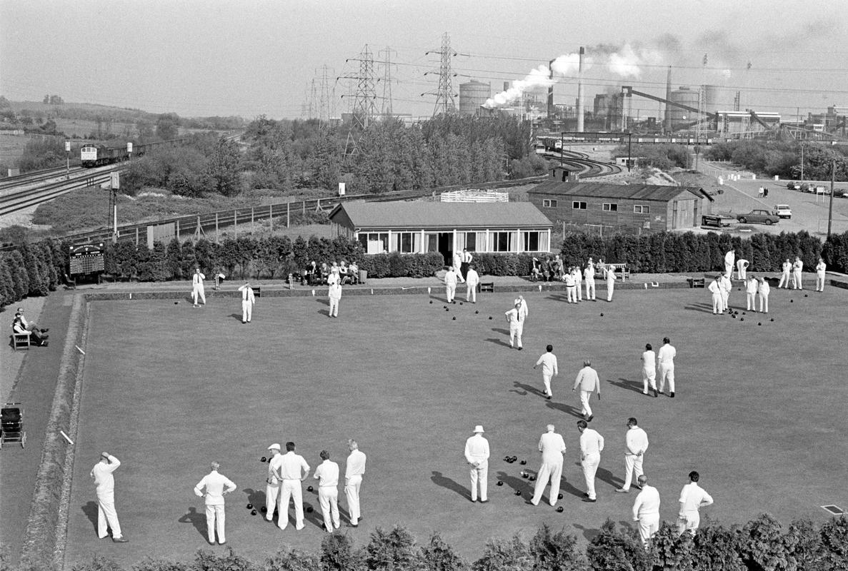 GB. WALES. Newport. The contrast between the healthy activity of Newport Bowling Club, all wearing their whites battling the dirt and pollution of Llanwern steel works in the background. 1971.