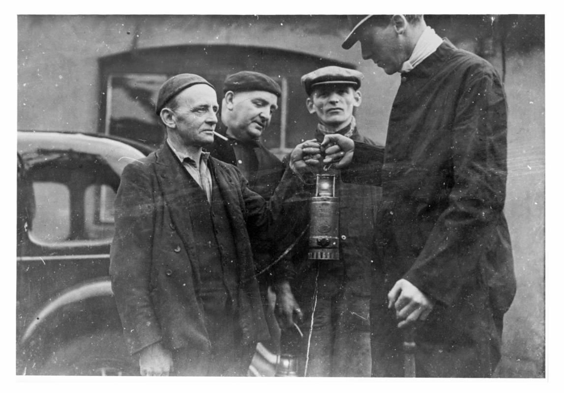 Four men with electric hand lamp. Supposed to be the first electric hand lamp in use at Big Pit.