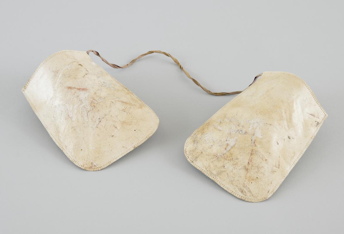 Pair of cream oven gloves,  &#039;leatherette&#039; material, attached together with linen strap. Image shows upper side of gloves. Well used, stained and scuffed.