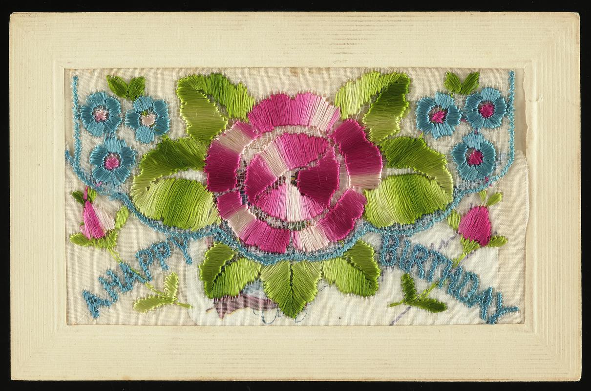 Embroidered silk postcard inscribed A Happy Birthday. Sent from France possibly by Tom Hardiman during First World War. Undated. Embroidered with large pink and white rose with smaller blue flowers. Flap opening contains a small card with an image including flags, and printed with words To my Dear Sweetheart (Sweetheart has been crossed out by hand and replaced with Friend). No message on back.
