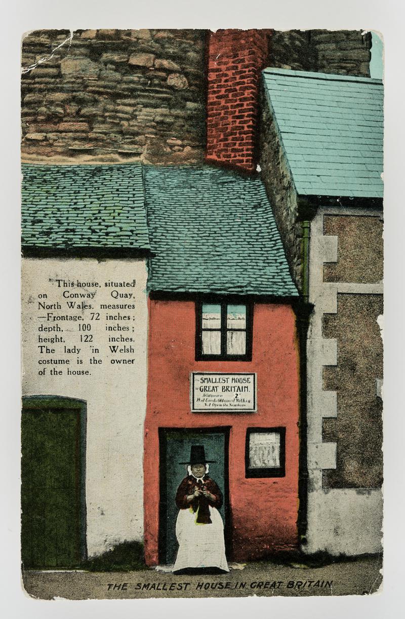 Lady in Welsh costume (the owner) knitting outside the smallest house in Great Britiain, at Conway, Caerns..