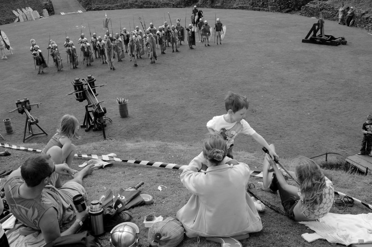 GB. WALES. Caerleon. Military spactacular. Caerleon Roman Ampitheatre. The Ermine Street Guard re-enactment society parade in the orignal ampitheatre. A young tourist attempts to kill his sister to get into the spirit of the occasion. 2009.