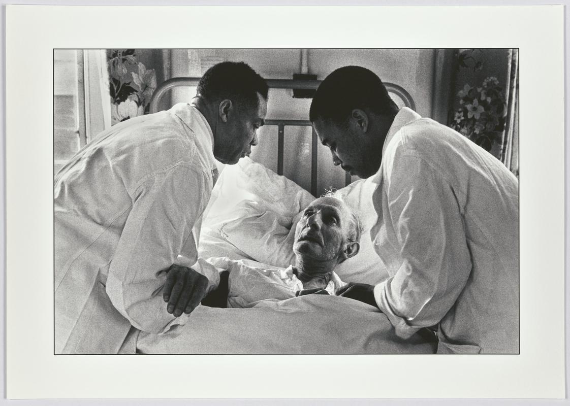 An elderly white patient wakes up in a hospital to find two black male nurses tending him. Midlands, England
