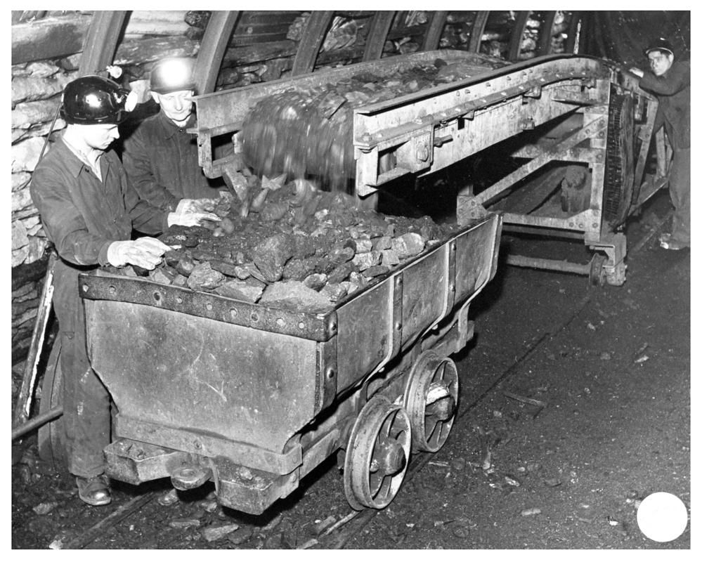 Trainee being shown coal being loaded from a conveyor into a dram