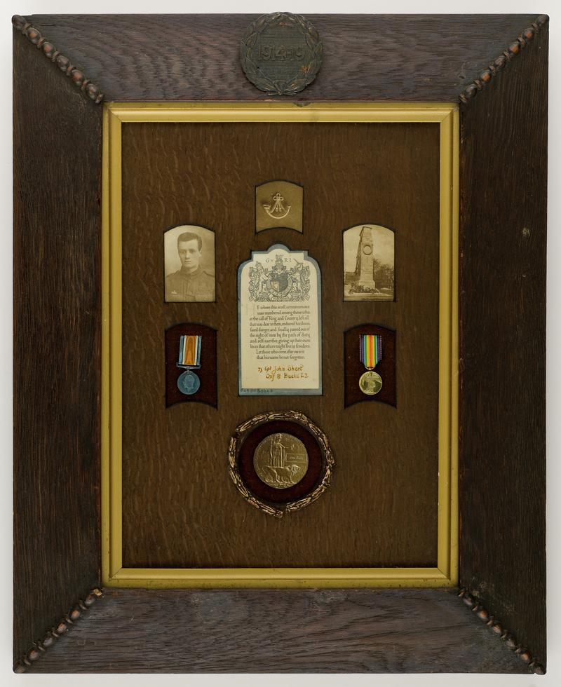 Framed photographs, medals, a bugle and a certificate commemorating Lance-Corporal John Short of the Oxfordshire and Buckinghamshire Light Infantry. Top of the frame features a carved inscription &#039;1914 - 1919&#039; within a wreath.