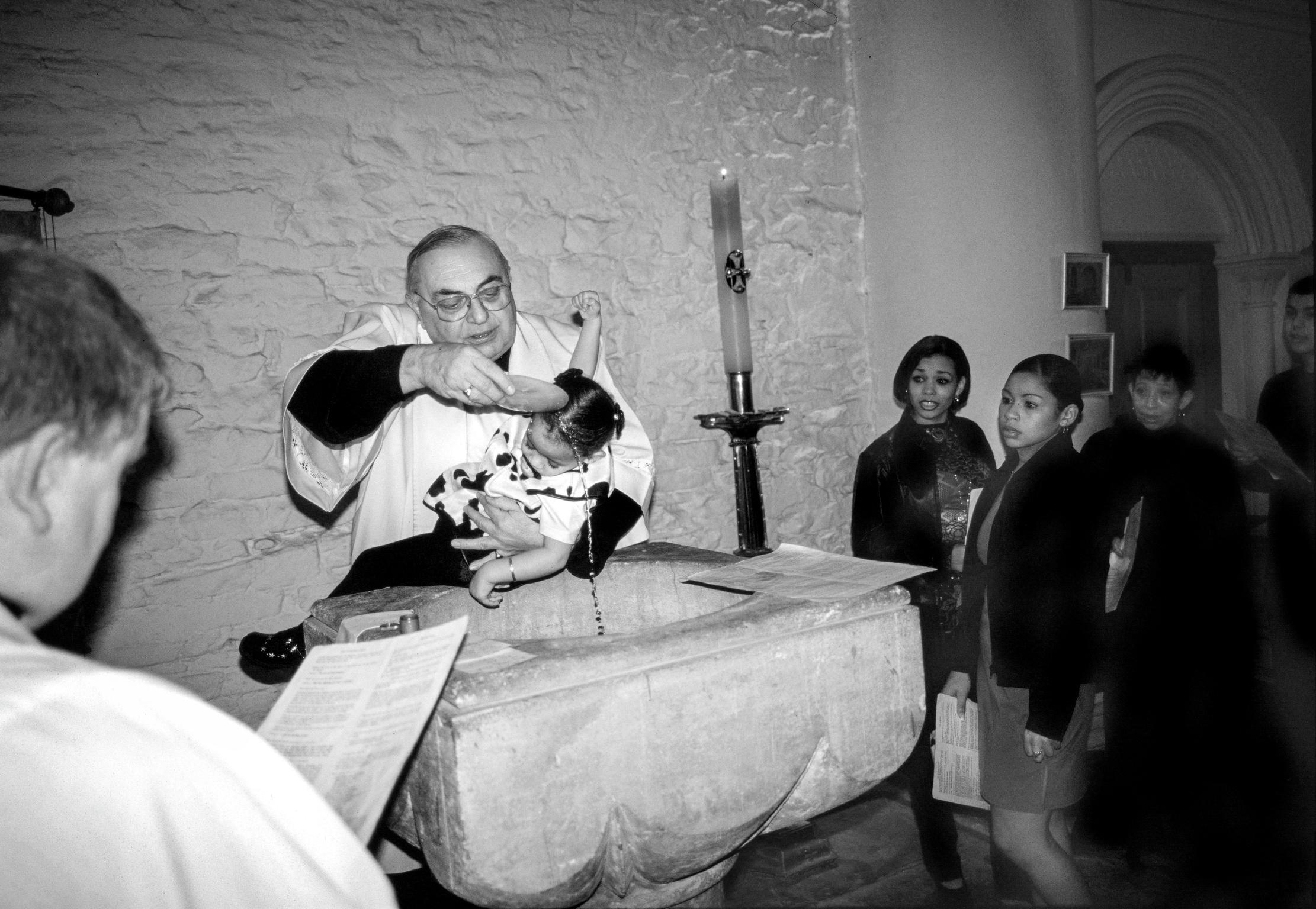Father Jordon baptising a local child at St Mary's Church, Butetown. Cardiff, Wales