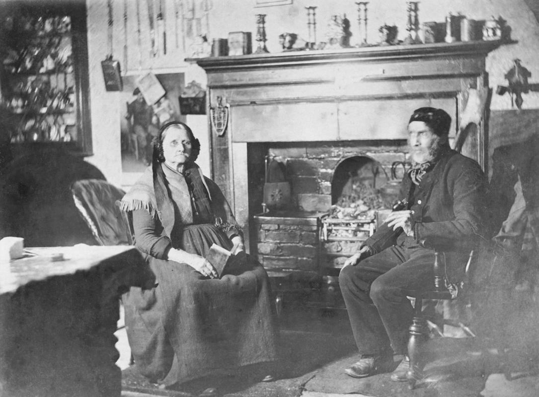 Photograph of elderly couple sitting in front of a fireplace.