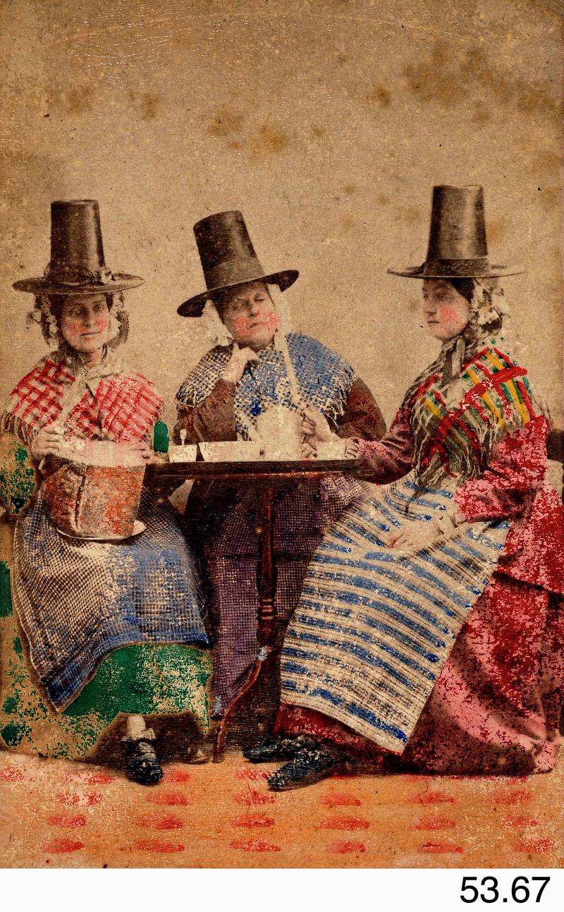 Tinted photograph of 3 women in Welsh costume having tea