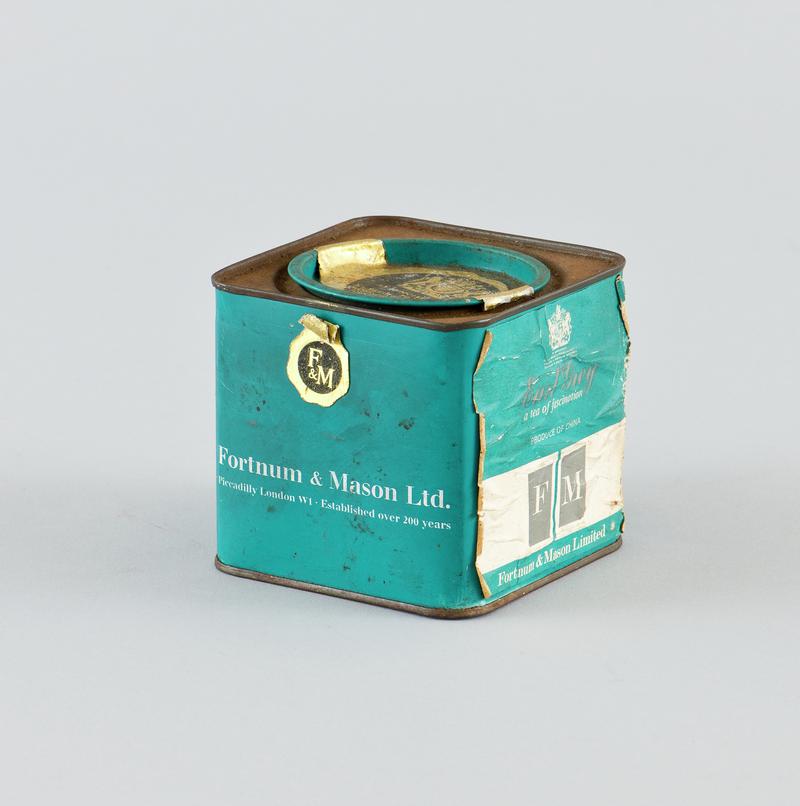 Square tin with teal and white paper label attached around body, with teal circluar lid at center of the top which has paper royal warrant label. That once contained Fortnum &amp; Mason loose Early Grey tea.