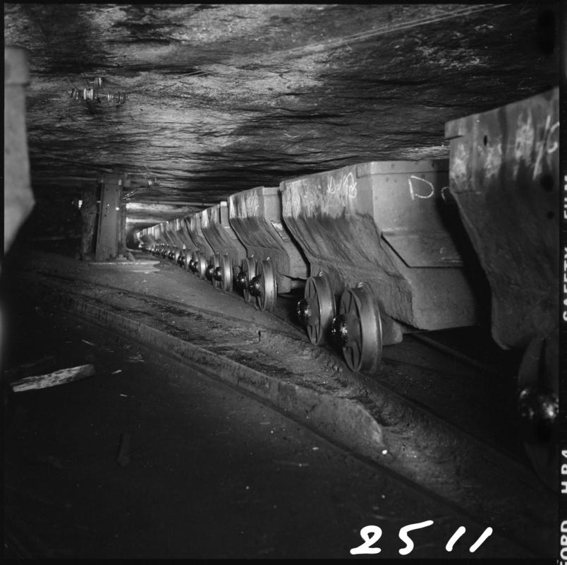 Black and white film negative showing a line of drams in the Graigola Seam, Graig Merthyr Colliery.  Note the unsupported sandstone roof.  &#039;Graig Merthyr&#039; is transcribed from original negative bag.