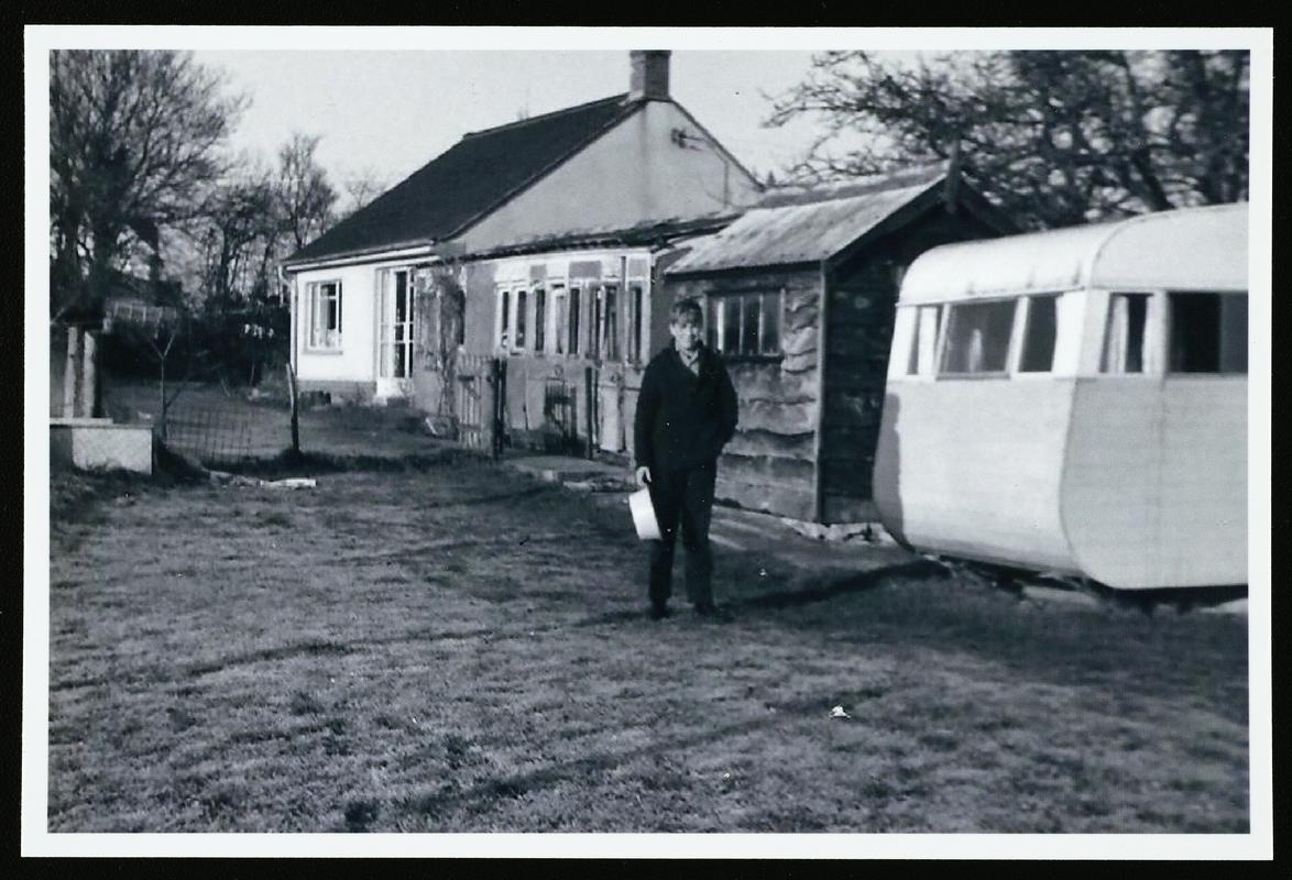 Black and white photograph of Cambrian Railways brake/3rd carriage body of c.1890 (acc.no. 87.116I) grounded at Ashcott, Somerset, prior to donation to AC-NMW. Carriage is at centre, with with bungalow to left, and shed and caravan to right, c.1968.