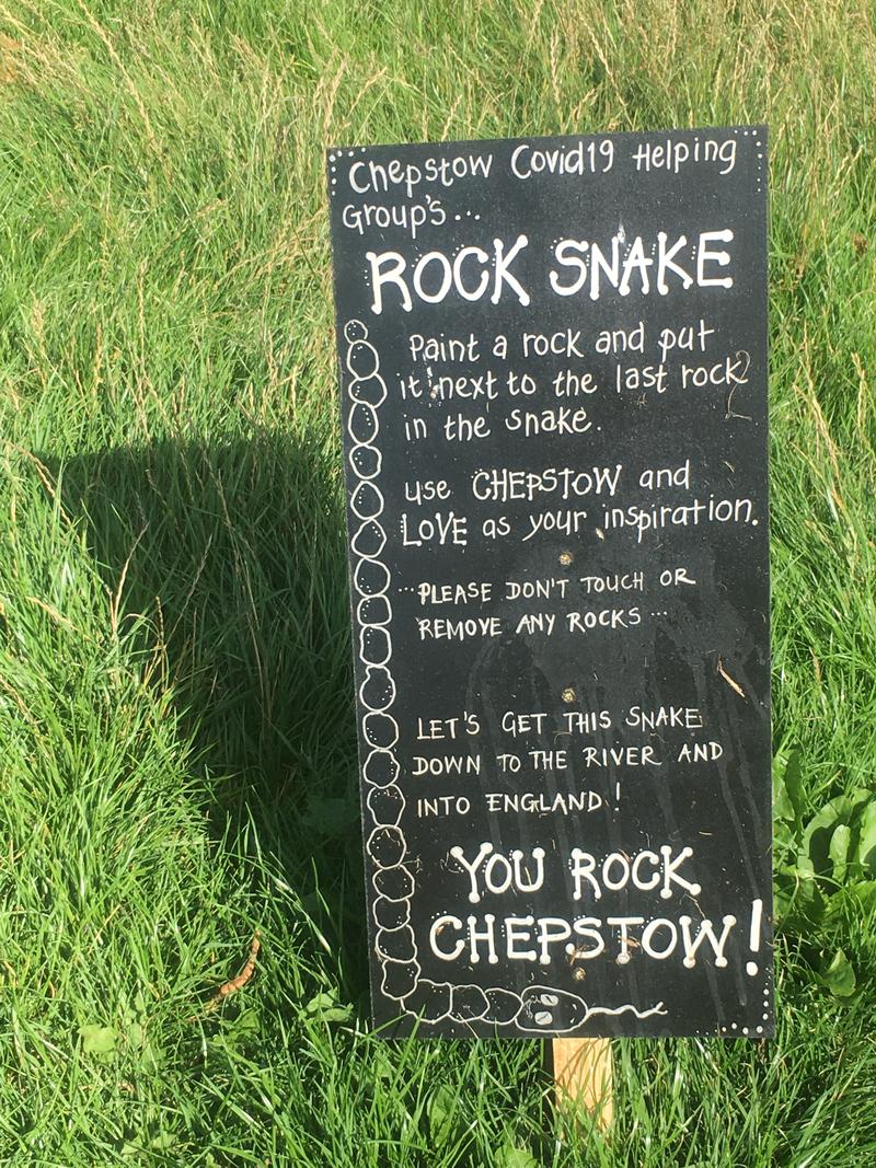Sign near the start of the line of painted pebbles in Castle Dell, Chepstow, Monmouthshire. Reading &#039;Chepstow&#039;s Covid 19 Helping Group&#039;s Rock Snake Paint a rock and put it next to the last rock in the snake. Use Chepstow and Love as your inspiration. Please don&#039;t touch or remove any rocks ... Let&#039;s get this snake down to the river and into England! You Rock Chepstow!&#039;