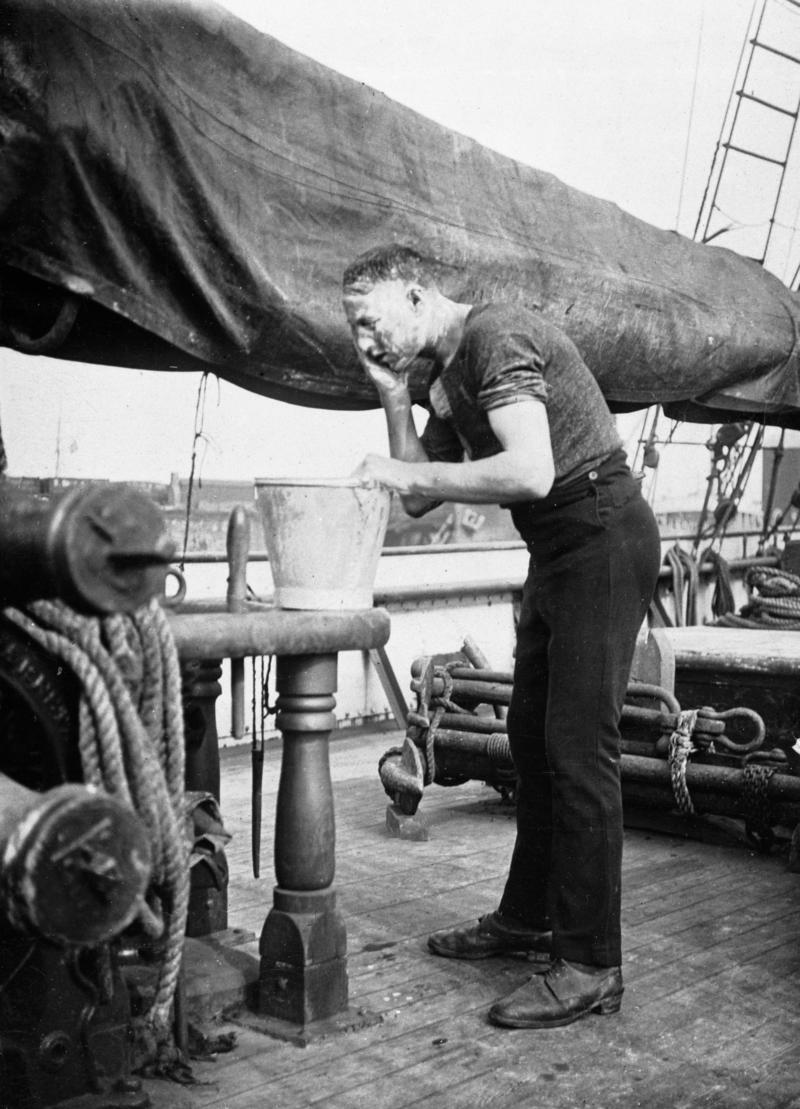 A sailor washing his face from a bucket of water.