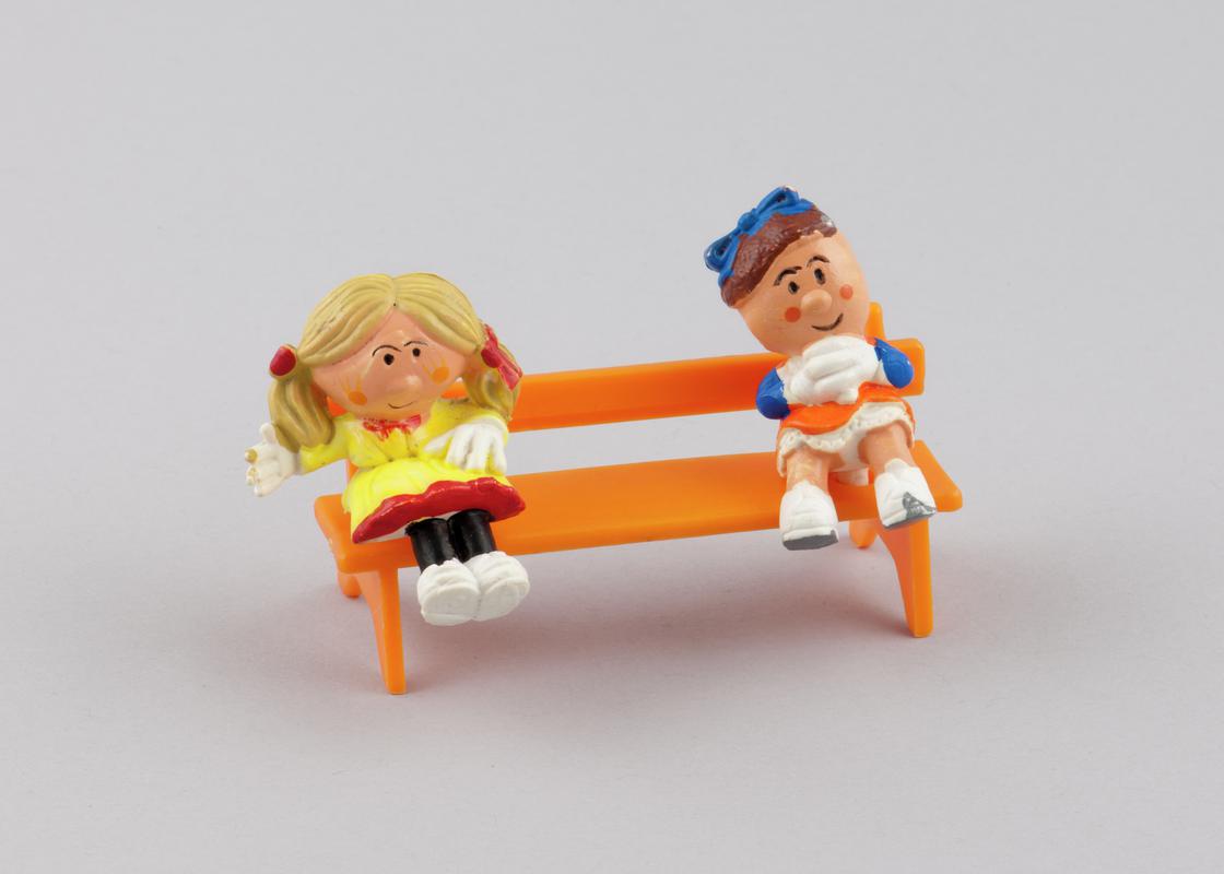 Sitting model of character Rosalie (2000.179/6) from the Magic Roundabout &amp; Sitting model of character Florence (2000.179/7)  from the Magic Roundabout.Model of orange plastic bench (2000.179/14) with two holes on seat for figures from the Magic Roundabout to be inserted.