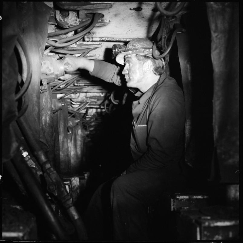 Black and white film negative showing an engineer carrying out maintenance work on the Gullick Dobson powered supports, underground at Merthyr Vale Colliery.