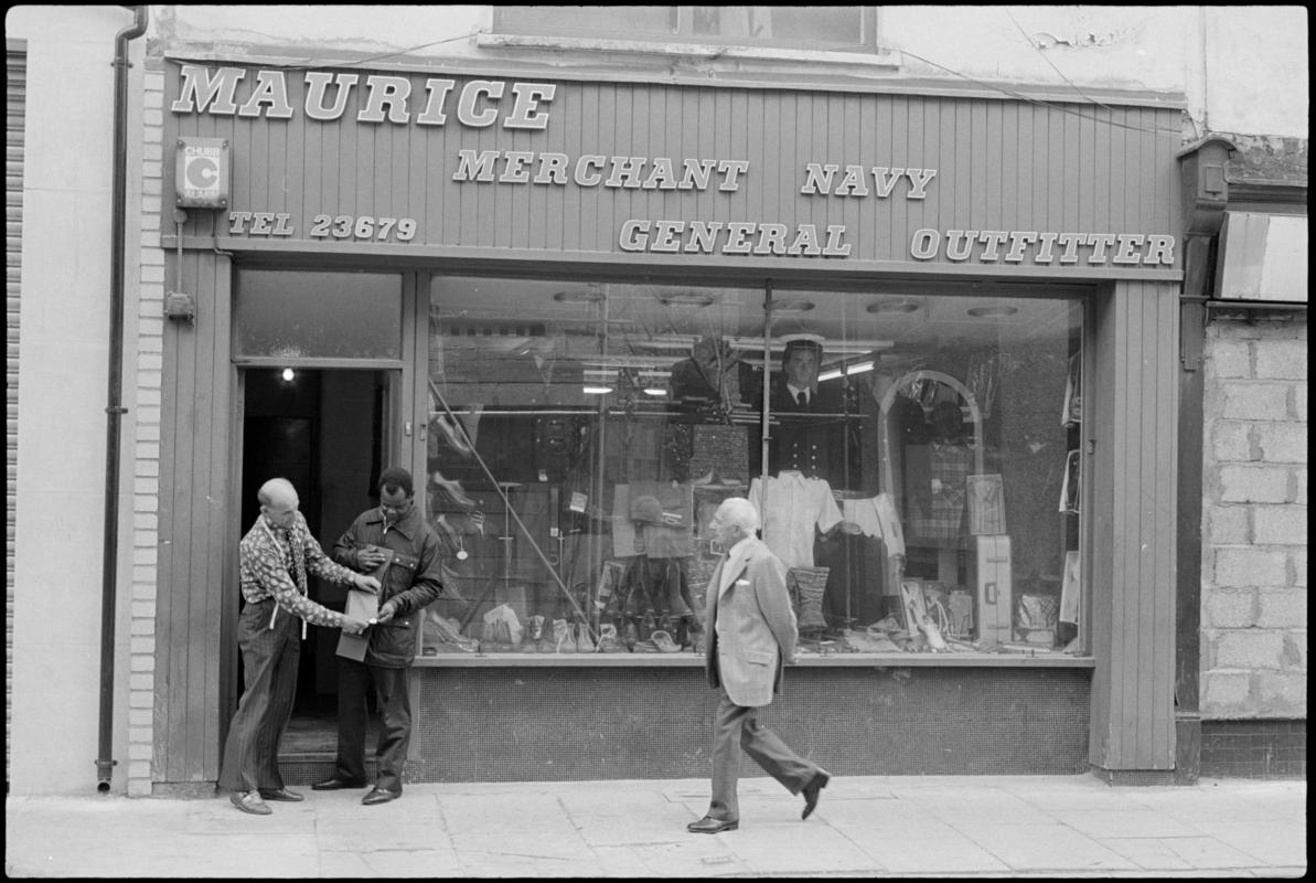 Exterior view of &#039;Maurice Merchant Navy General Outfitter&#039;, 5 James Street, Butetown, showing the proprietor Mr M. Colpstein assisting a customer.