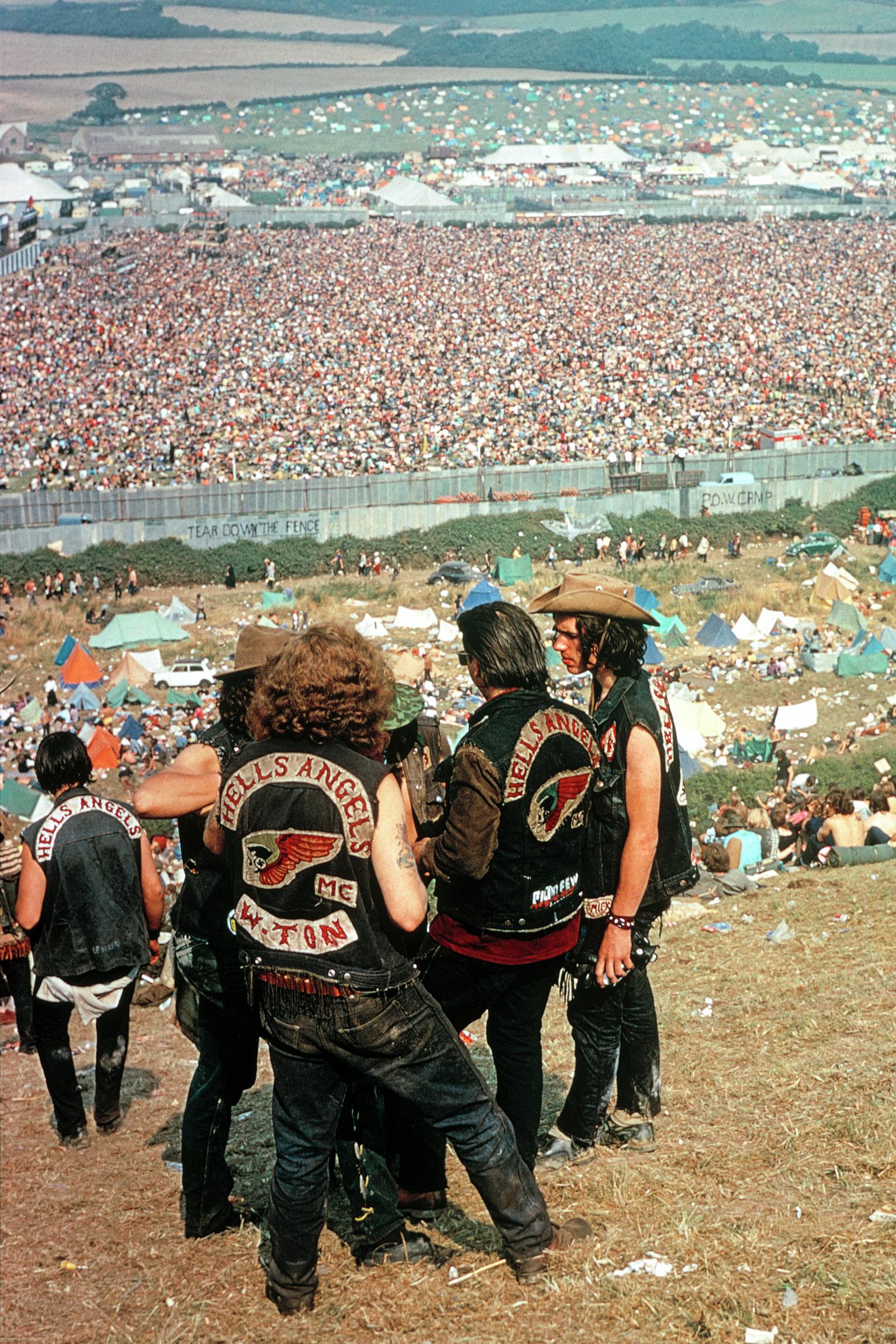 Isle of Wight Festival. A group of Hells Angels, relegated from their usual role of security, stand lonely aloof from the festival