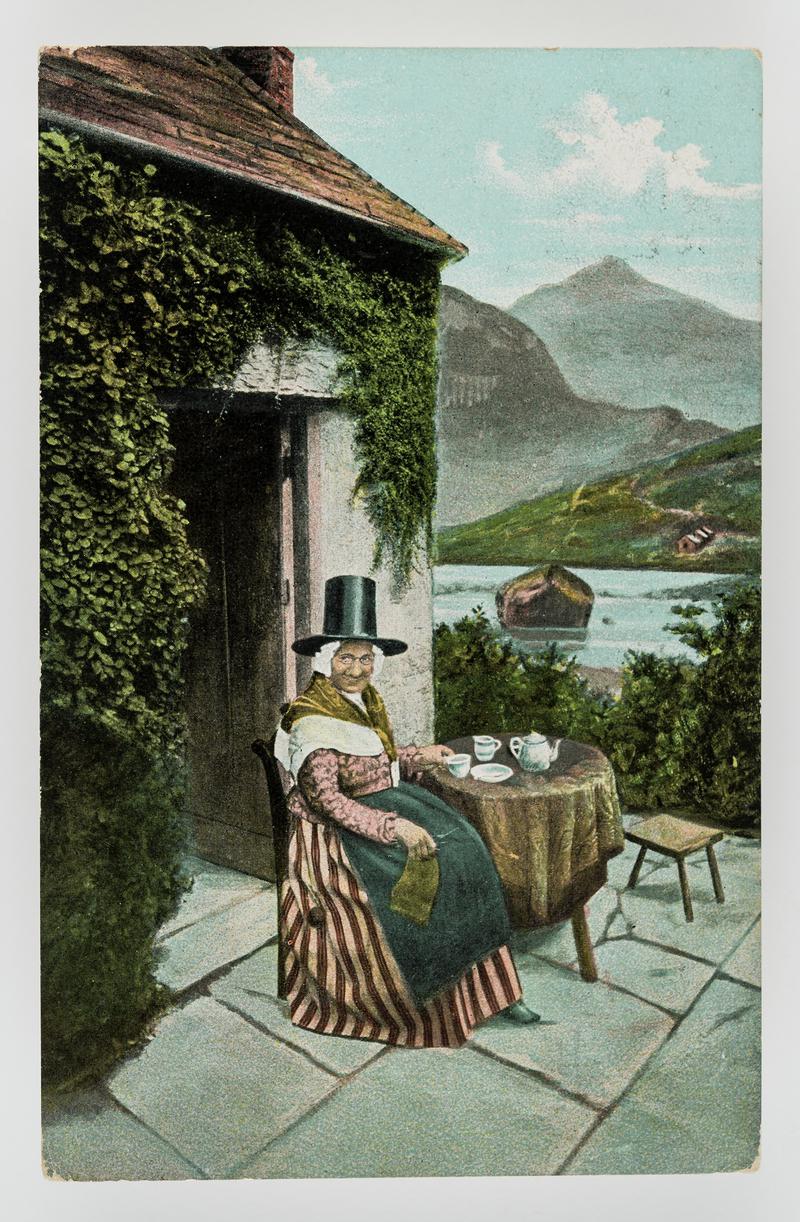 Old lady in Welsh costume taking tea outside her cottage.  Postmark:  Treharris