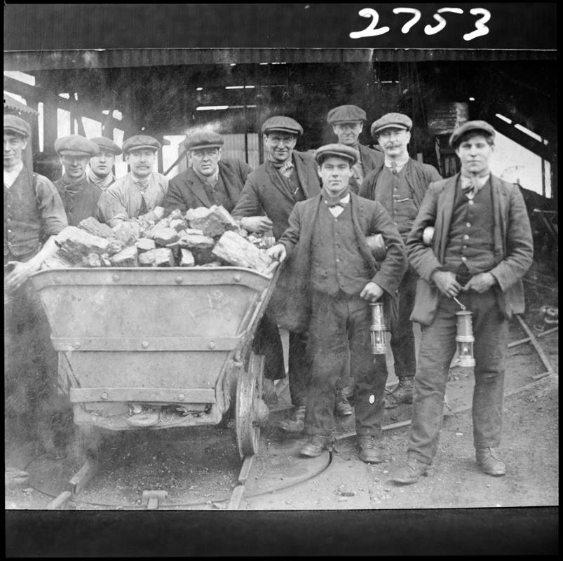 Black and white film negative of a photograph showing a group of miners gathered around a coal dram. &#039;Men with Tram&#039; is transcribed from original negative bag.