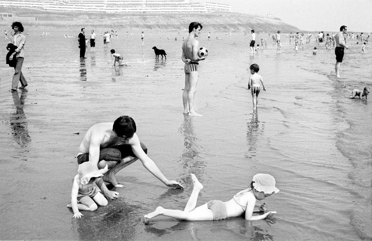 GB. WALES. Barry Island. General. A father with his children relax on the beach at Barry Island, South Wales.  The picture is during the &#039;miners&#039; week&#039; the holiday period of the miners of South Wales.  It is probable that most of the people on the beach are miners on their holiday.  Due to the closing of the pits this cultural happening no longer takes place. 1973