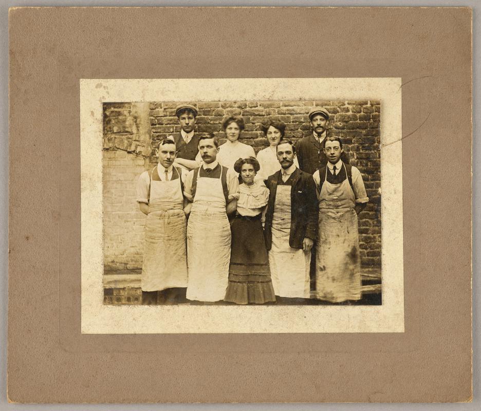 Group photograph of 3 women and 6 men, most men are wearing aprons. Mounted on paper then card.