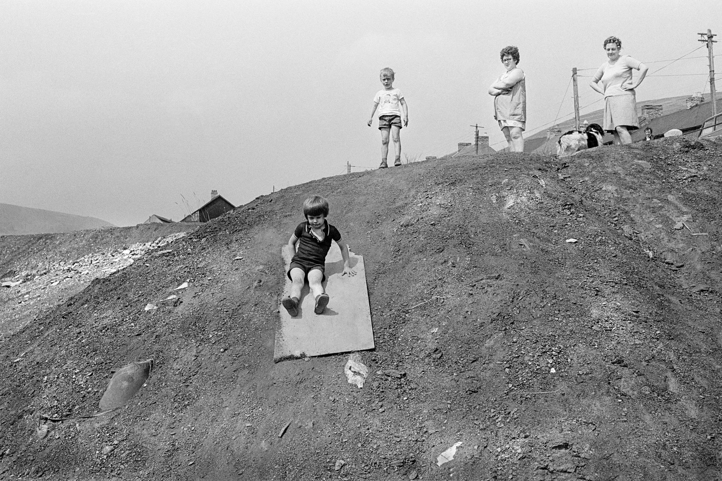 Children make a wooden board into a sledge to slide down a slag tip side. Abertillery, Wales