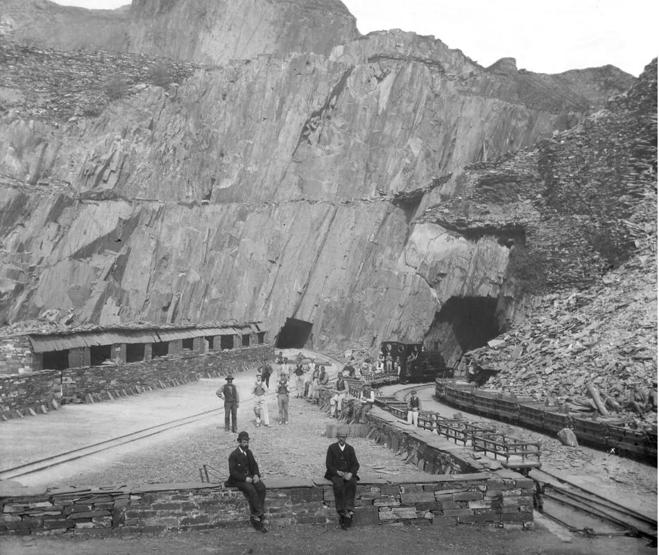 View of one of the &#039;ponciau&#039; (galleries) at Dinorwic Quarry, showing quarrymen, gwaliau, and  a steam locomotive hauling slate loader wagons