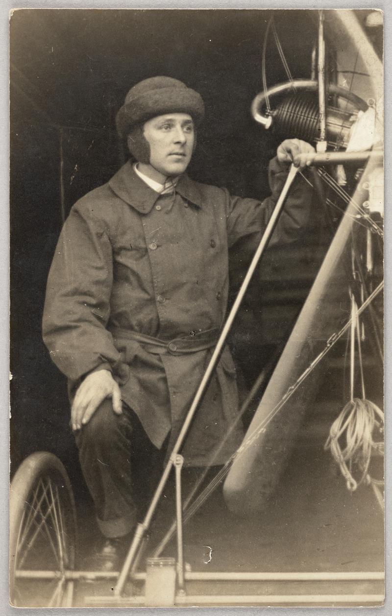 View of C.H. Watkins wearing fur helmet standing next to aeroplane. Printed on a postcard.