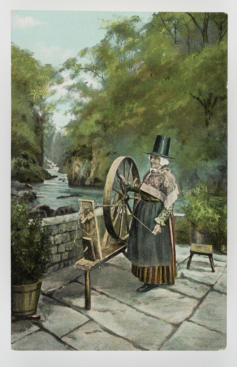 Woman in Welsh costume standing next to a spinning wheel - river in background