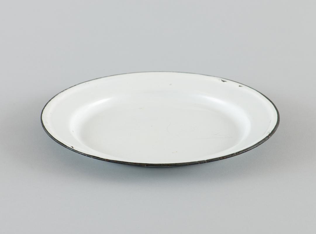 White enamelware plate, with black rim. Chipped in places.