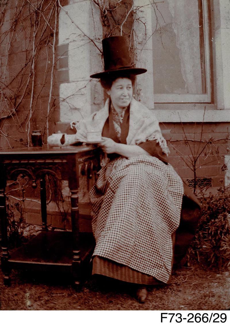 Photograph of a women in Welsh costume drinking tea outdoors