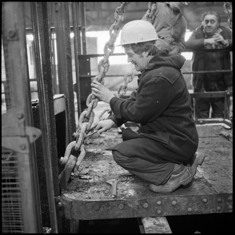 Black and white film negative showing man carrying out maintenance work on top of cage at pit top, Big Pit Colliery January 1982.  &#039;Big Pit Blaenavon Jan 1982&#039; is transcribed from original negative bag.