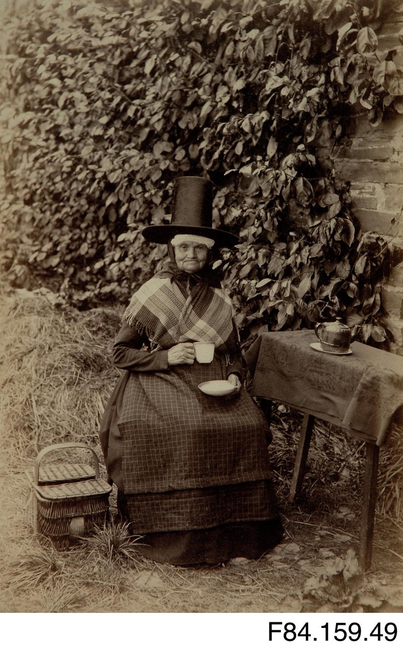 Mounted photograph of a woman in Welsh costume drinking tea