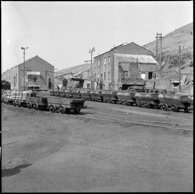 Black and white film negative showing Graig Merthyr Colliery yard in 1977 with a long journey of drams waiting to be run into the mine.  In the foreground are special cut-down drams used for moving supplies.  &#039;Graig Merthyr&#039; is transcribed from original negative bag.